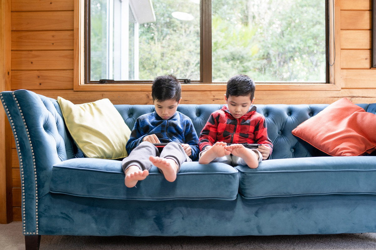 Two boys sitting on a blue couch looking at handheld devices