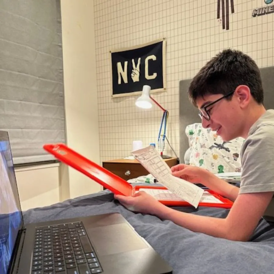 A YSA student at home with a laptop, reading a D&D character sheet